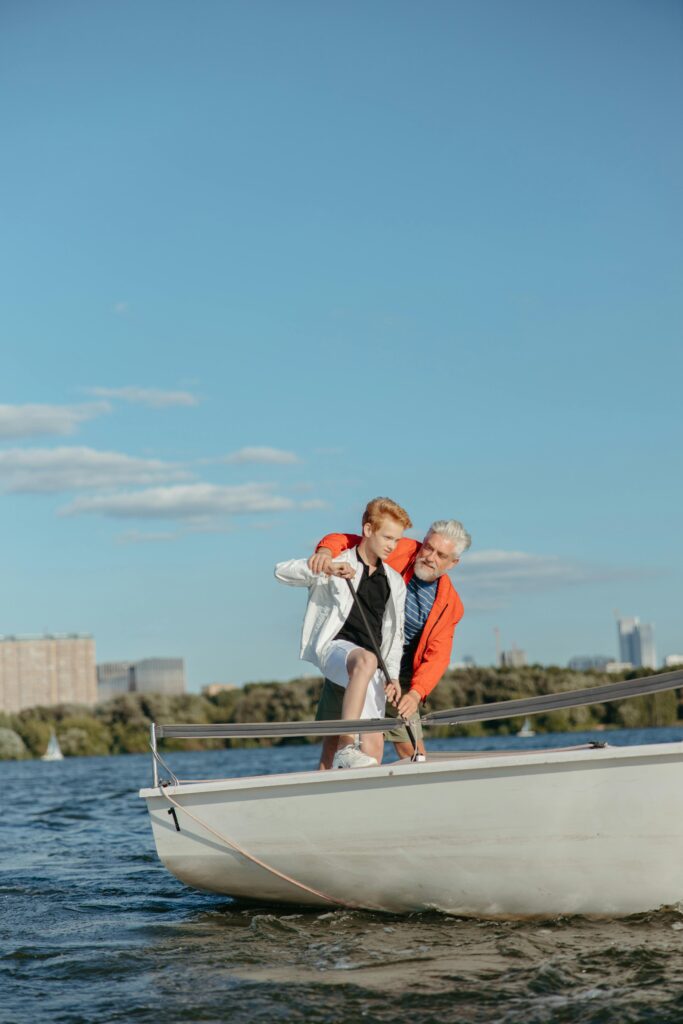 Elderly man and teenage boy enjoying sailing on a sunny day, bonding on a sailboat.